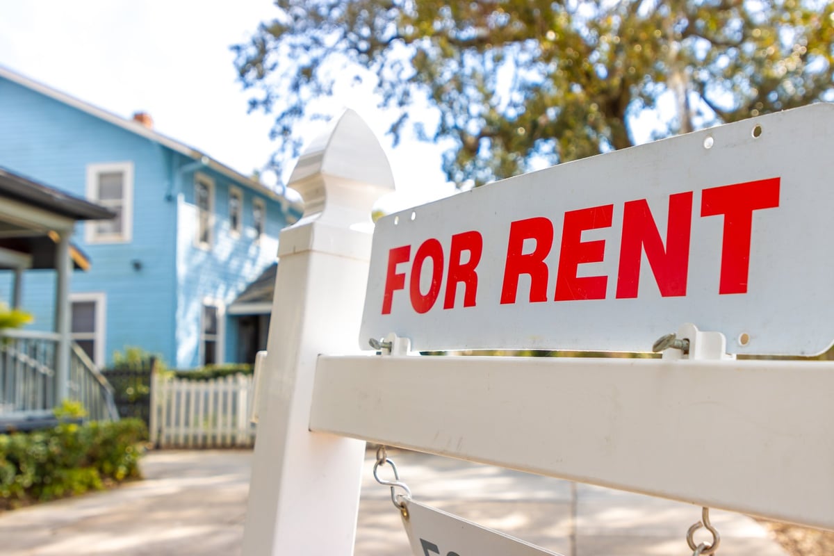 A white and red sign advertises a house for rent.