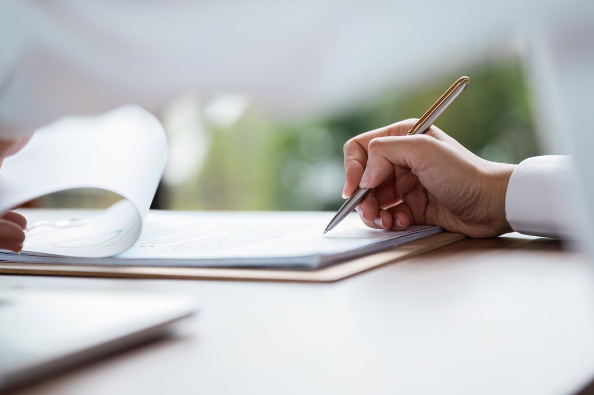 Close-up of a hand signing a business contract with a pen on a desk, symbolizing agreement and professional commitment