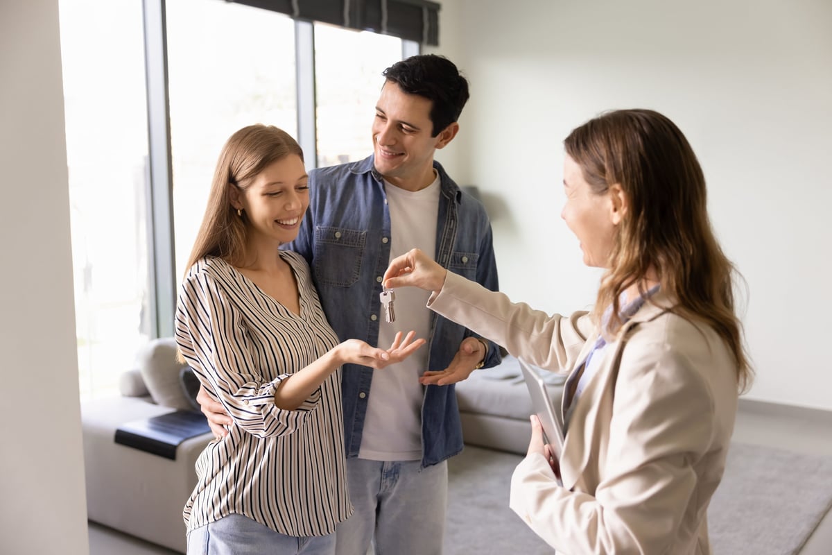 Real estate agent handing house keys to a happy couple after their financing was approved