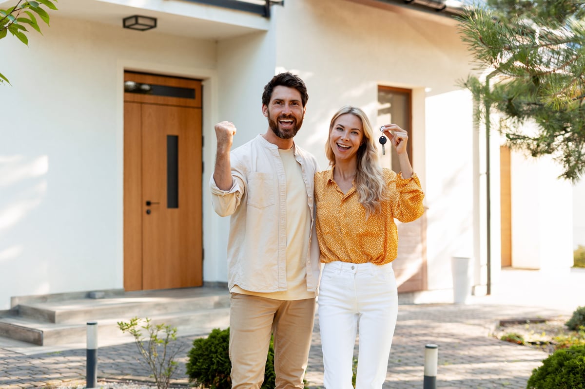 Excited couple celebrating their new home purchase, proudly displaying keys in front of their beautiful property