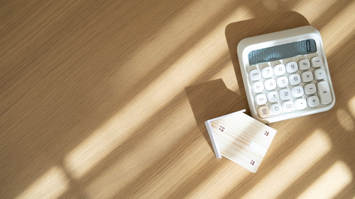Miniature house and calculator placed on wooden desk with light shadow background concept for mortgage loan housing finance investment and monthly payment planning.