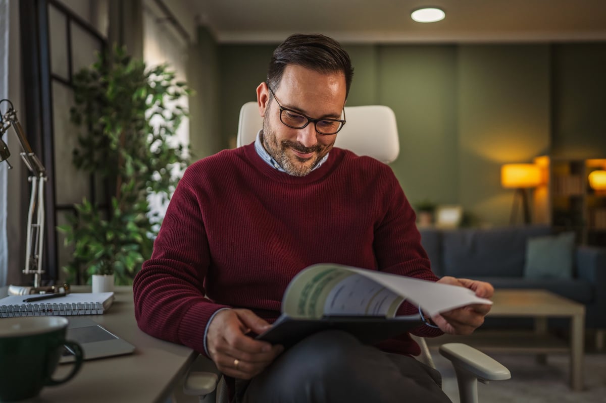 Man in home office reviewing financial reports and charts, focused on paperwork and data