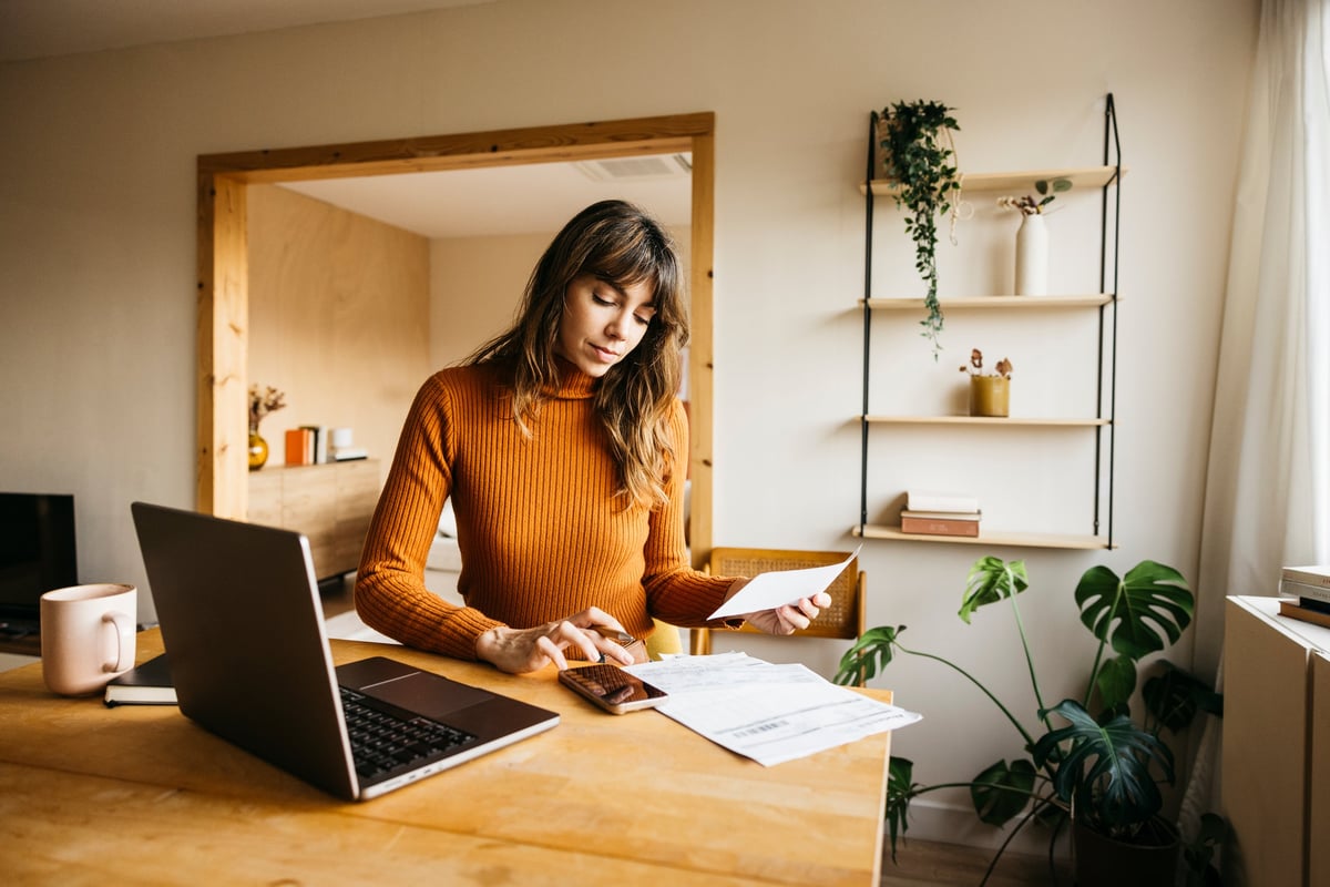 Woman calculating expenses using laptop and smartphone at a modern home office