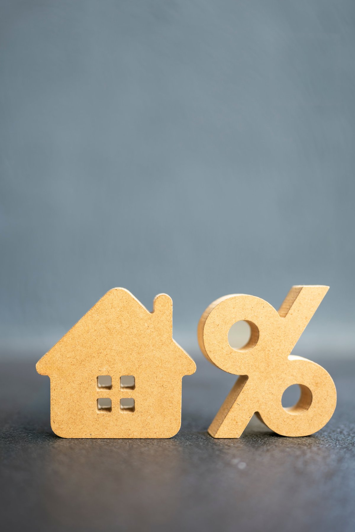 Wooden house model next to percentage symbol on table, representing mortgage interest rate, home loan, and property finance