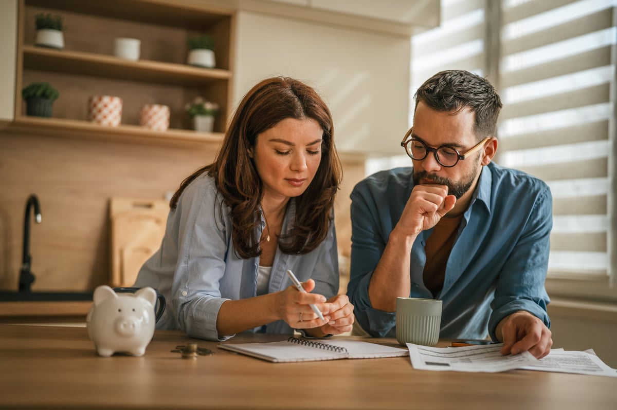 Couple reviewing paperwork and checking numbers together on a kitchen counter for financial planning