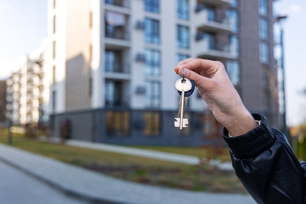 Hand holding house keys in front of a modern apartment building, symbolizing new home, rental, or property purchase