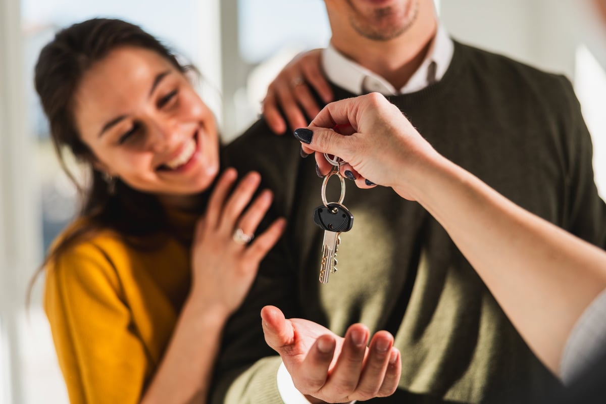 Real estate agent handing the keys of a bright new home to a first-time buyer couple