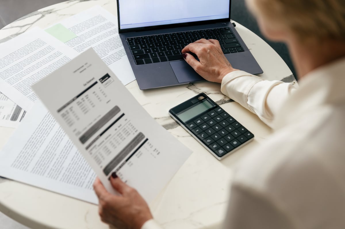 Woman analyzes financial documents and bank statements while seated at a table using a laptop
