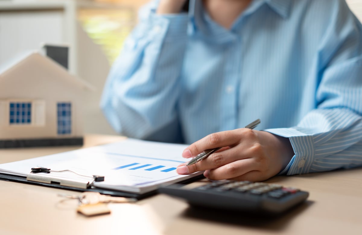 Businesswoman using calculator to review mortgage loan expenses and refinance plan, analyzing home budget, property interest, house financing, and broker cost calculations.