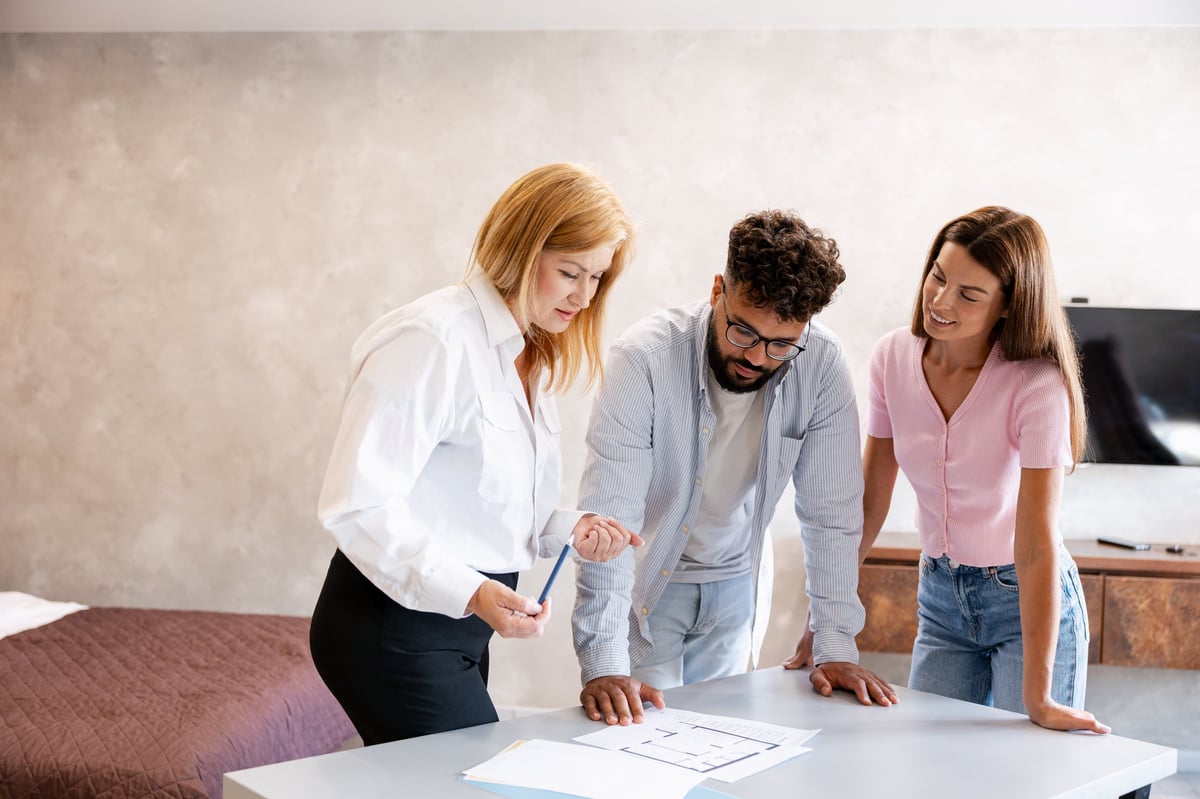 Real estate agent discussing home floor plans and property details with a young adult couple inside an apartment