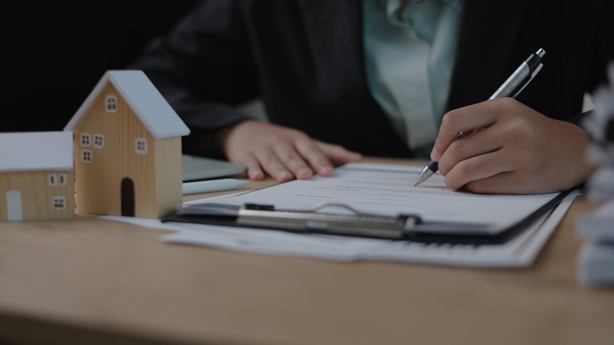 Business owner reviewing real estate purchase documents and a model house at a desk
