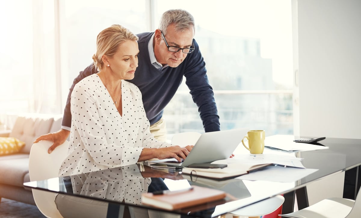 Shot of a mature couple using a laptop while going through paperwork at home
