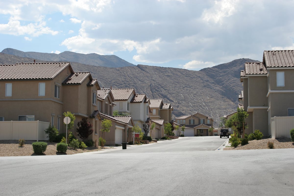 Suburban residential street with two-story stucco homes and tile roofs against desert mountain backdrop in Arizona