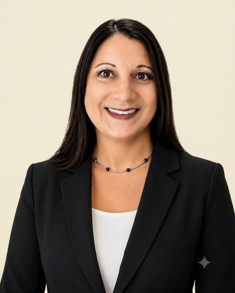 Professional headshot of a woman with long dark hair, wearing a black blazer and white top, smiling against a light beige background.