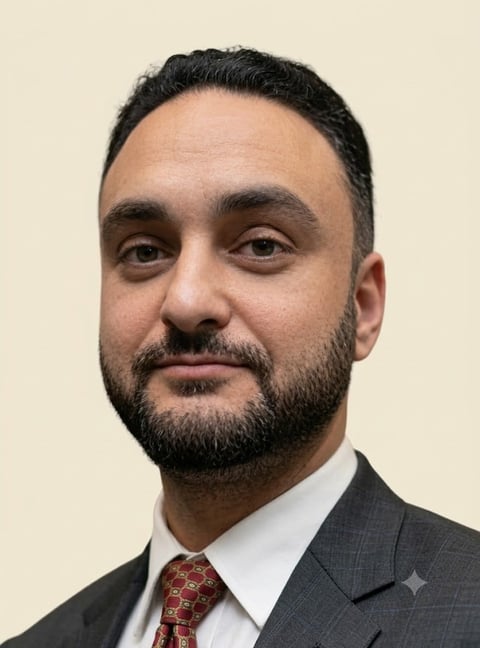 Professional headshot of a man with dark hair and beard wearing a gray suit jacket and red patterned tie against a beige background