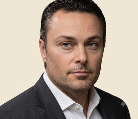 Professional headshot of a middle-aged man in a dark blazer and white shirt against a beige background