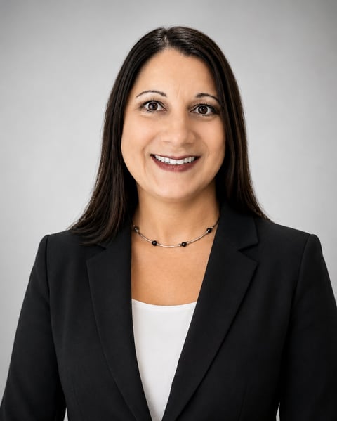 Professional headshot of a woman with long dark hair, wearing a black blazer and white top, smiling at the camera