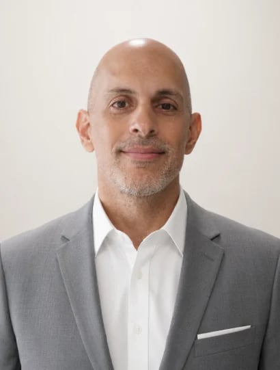 Professional headshot of a middle-aged man in a gray blazer and white shirt against a neutral background