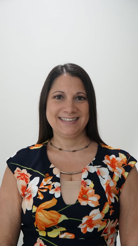 Woman with long dark hair smiling at camera, wearing a black floral dress with orange and white flowers
