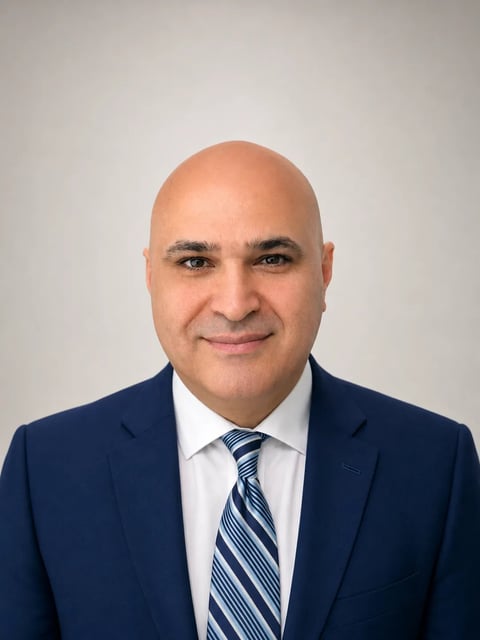 Professional headshot of a bald man wearing a dark blue suit, white dress shirt, and blue striped tie against a light gray background