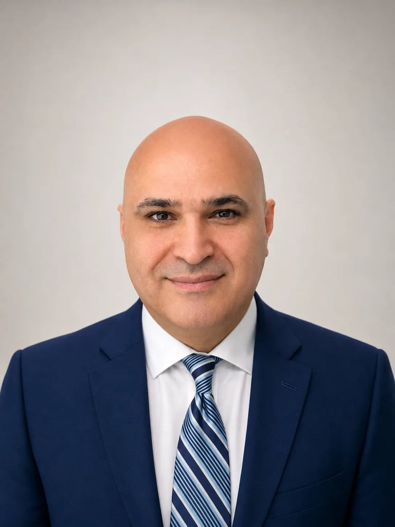 Professional headshot of a bald man wearing a dark blue suit, white dress shirt, and blue striped tie against a light gray background