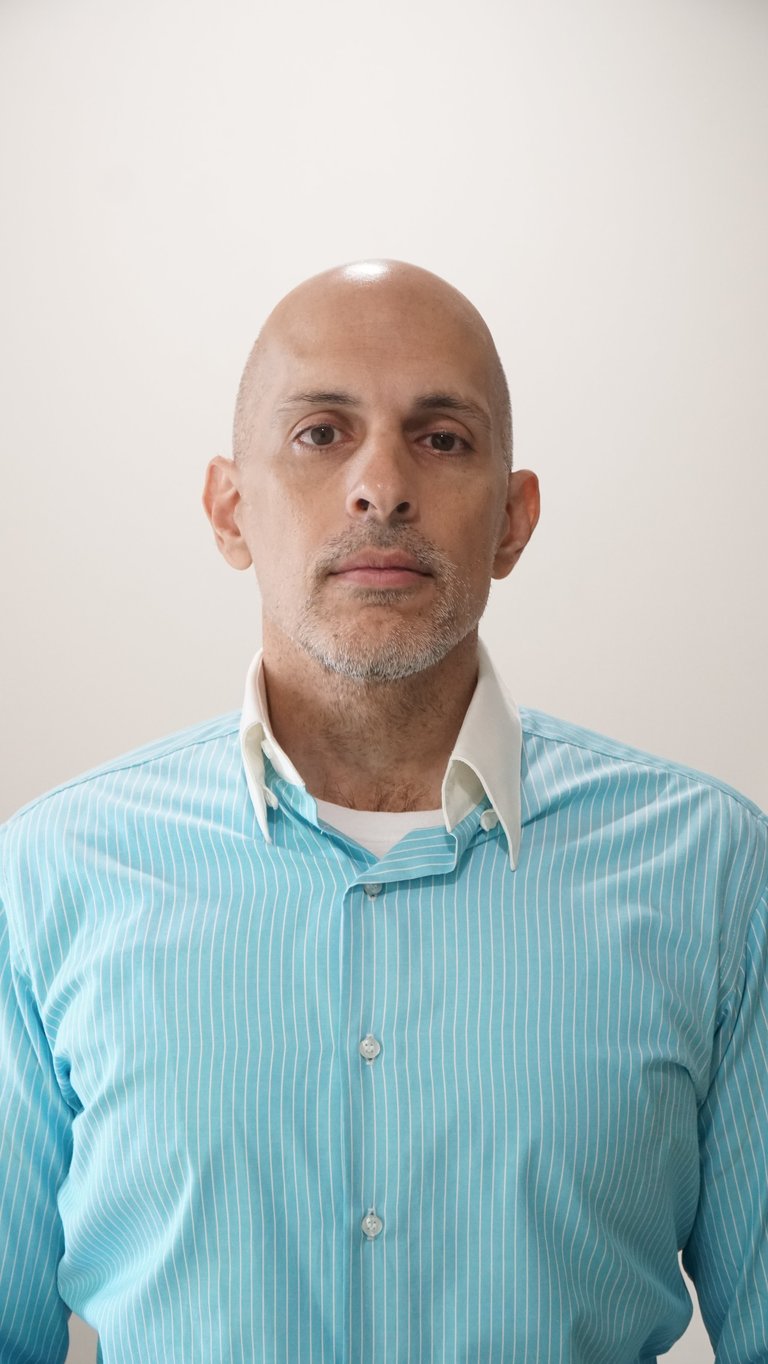 Professional headshot of a bald man with gray facial hair wearing a light blue pinstriped shirt against a white background