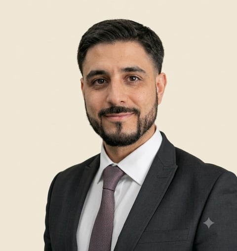 Professional headshot of a bearded man wearing a dark blazer, white shirt, and gray tie against a cream-colored background