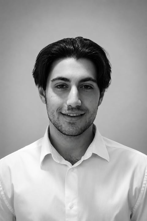 Black and white portrait of a smiling man with dark hair wearing a white collared shirt against a gray background