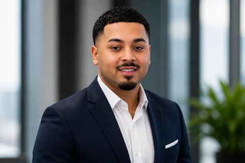 Professional headshot of a man in a navy blazer and white shirt against a modern office backdrop