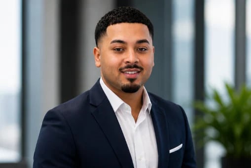 Professional headshot of a man in a navy blazer and white shirt against a modern office backdrop