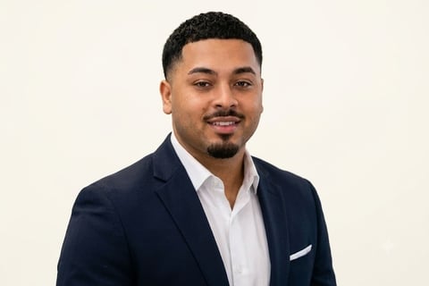Professional headshot of a man in a dark navy blazer and white shirt against a light background
