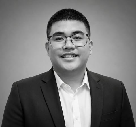 Portrait of an Asian man wearing glasses and a black blazer over a white shirt, smiling at the camera in black and white