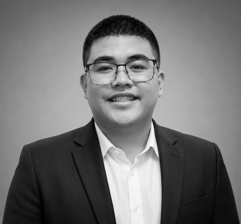 Portrait of an Asian man wearing glasses and a black blazer over a white shirt, smiling at the camera in black and white