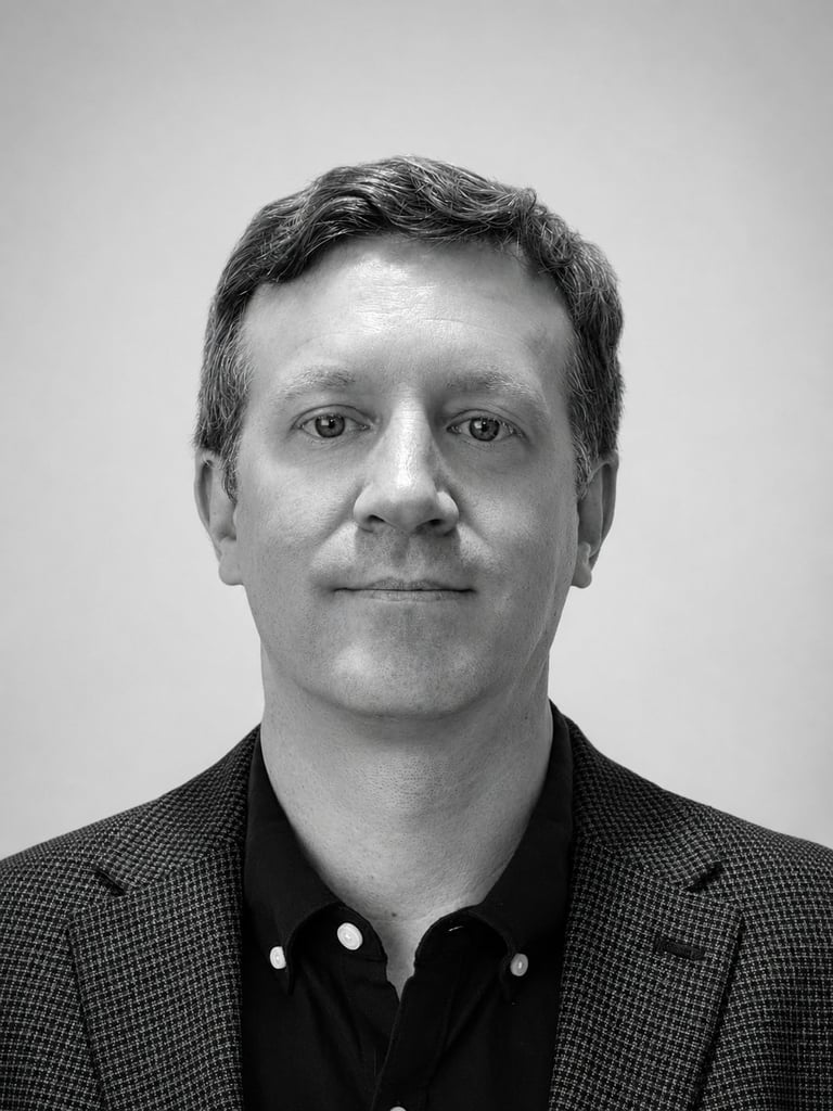 Black and white headshot portrait of a middle-aged man wearing a dark blazer and button-up shirt against a plain gray background