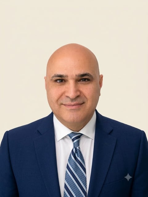 Professional headshot of a bald man in a dark blue blazer, white shirt, and blue striped tie against a neutral background