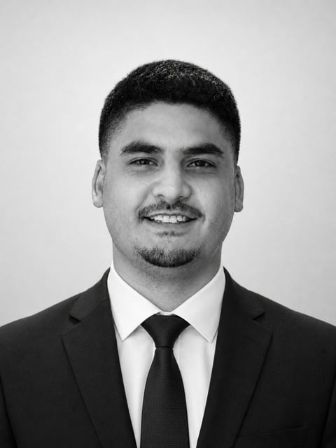 Black and white professional headshot of a man in business suit and tie, smiling at camera against neutral background