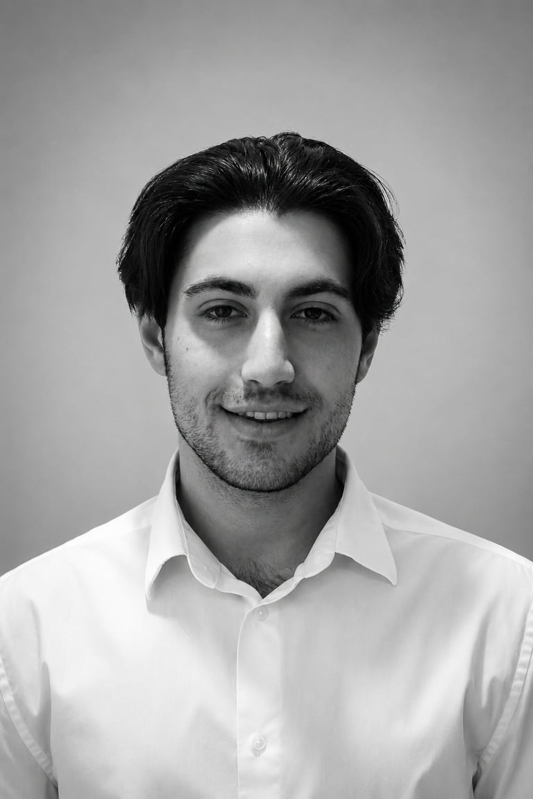 Black and white headshot of a man with dark hair wearing a white collared shirt, smiling at the camera against a gray background