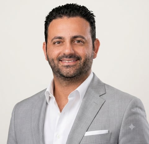 Professional headshot of a man wearing a light gray blazer and white shirt, smiling at the camera against a neutral background