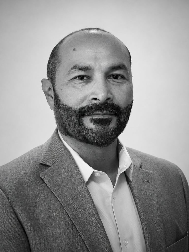Black and white headshot of a bearded man in a grey blazer and white shirt against a neutral background