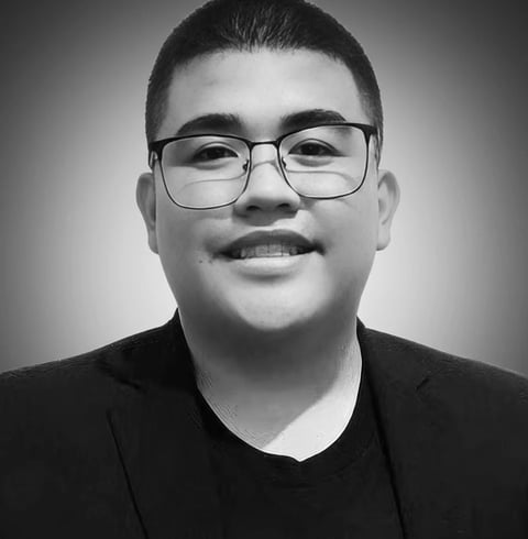 Black and white portrait of a smiling person wearing glasses and a dark shirt against a neutral background